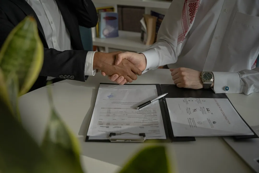 Two people shaking hands over signing documents at a business deal closing