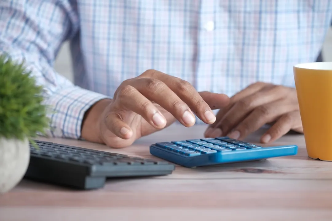 Business owner signing loan documents at desk with calculator and financial papers