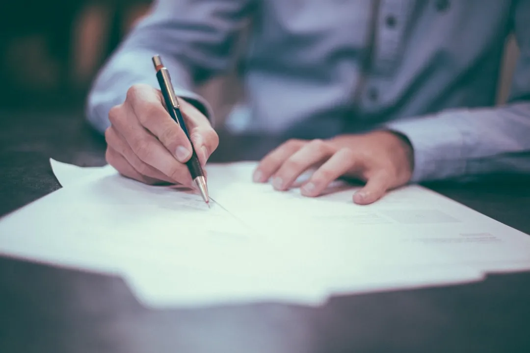 Close-up of a person writing on legal documents with a pen during a business deal